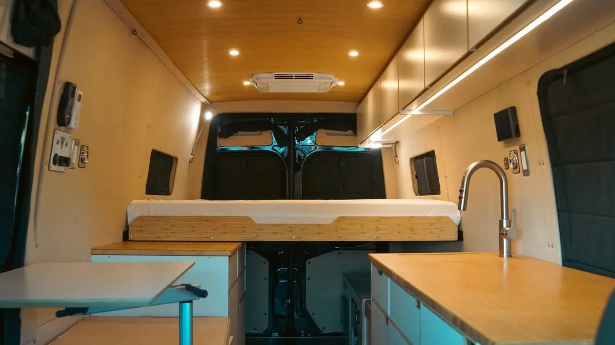 RV furniture - Fixed rear bed, built-in bench, fold-out table, and galley cabinets inside a Vansmith Sprinter Duo XL