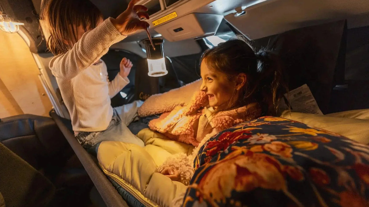 How to wash a sleeping bag - Two kids in sleeping bags on the cab bunk of a Vansmith camper van with a lantern