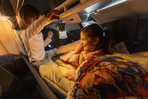 How to wash a sleeping bag - Two kids in sleeping bags on the cab bunk of a Vansmith camper van with a lantern