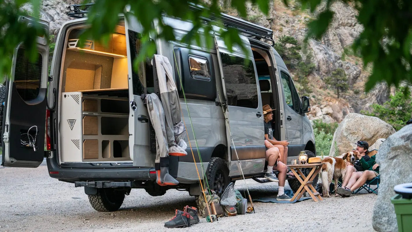 Couple Sitting on Side of The Vansmith Duo XLS Van Conversion with Picnic Table and Fishing Gear Outside