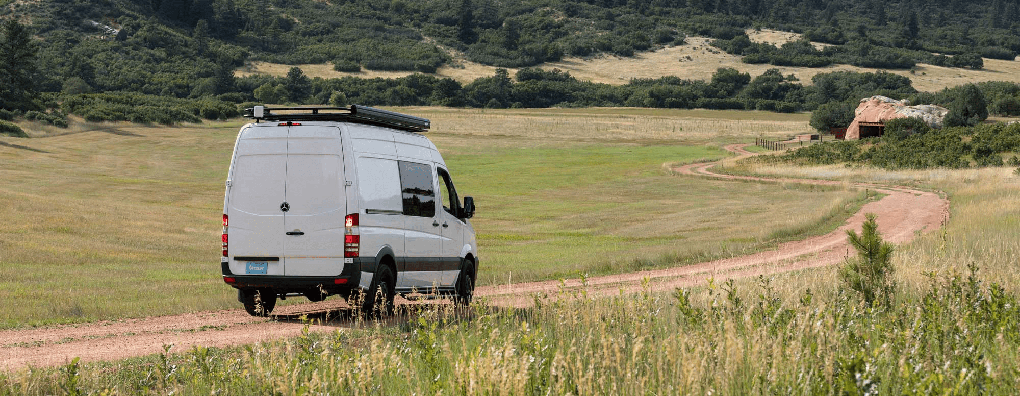 Back of Eco Friendly Sprinter Van Conversion by The Vansmith Driving on Dirt Road Through Large Field