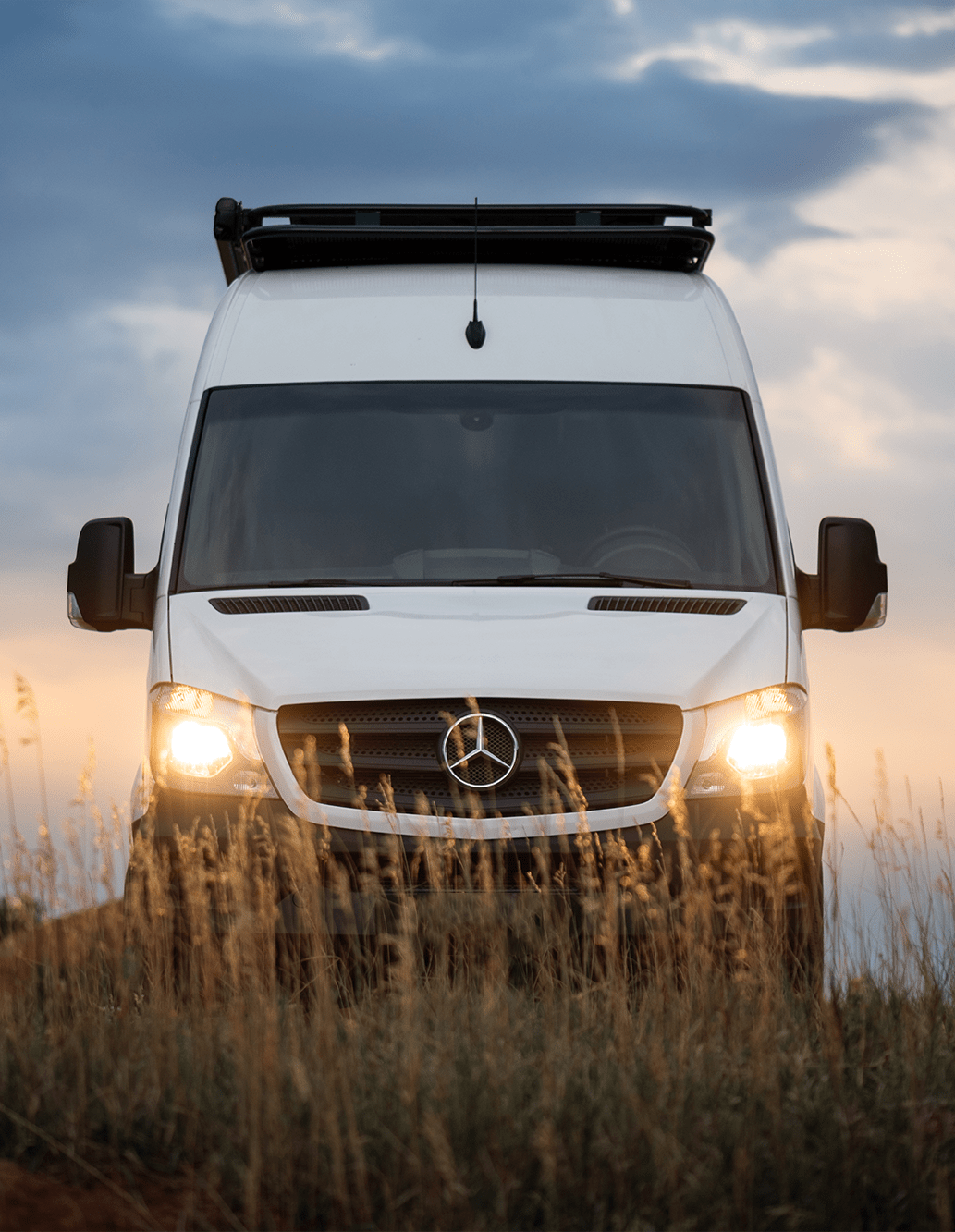 Front of Colorado Sprinter Van Conversion by The Vansmith with Headlights Shining Through Reedgrass