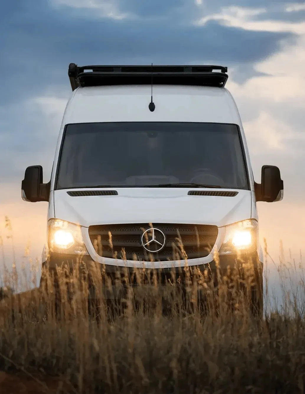 Front of Colorado Sprinter Van Conversion by The Vansmith with Headlights Shining Through Reedgrass
