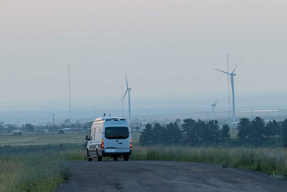 Sustainable Sprinter Van Conversion by The Vansmith Driving Past Wind Power Turbines