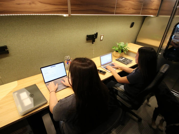 Two people working at facing desks inside the Hustle - The XL Work Van mobile office conversion - The Vansmith