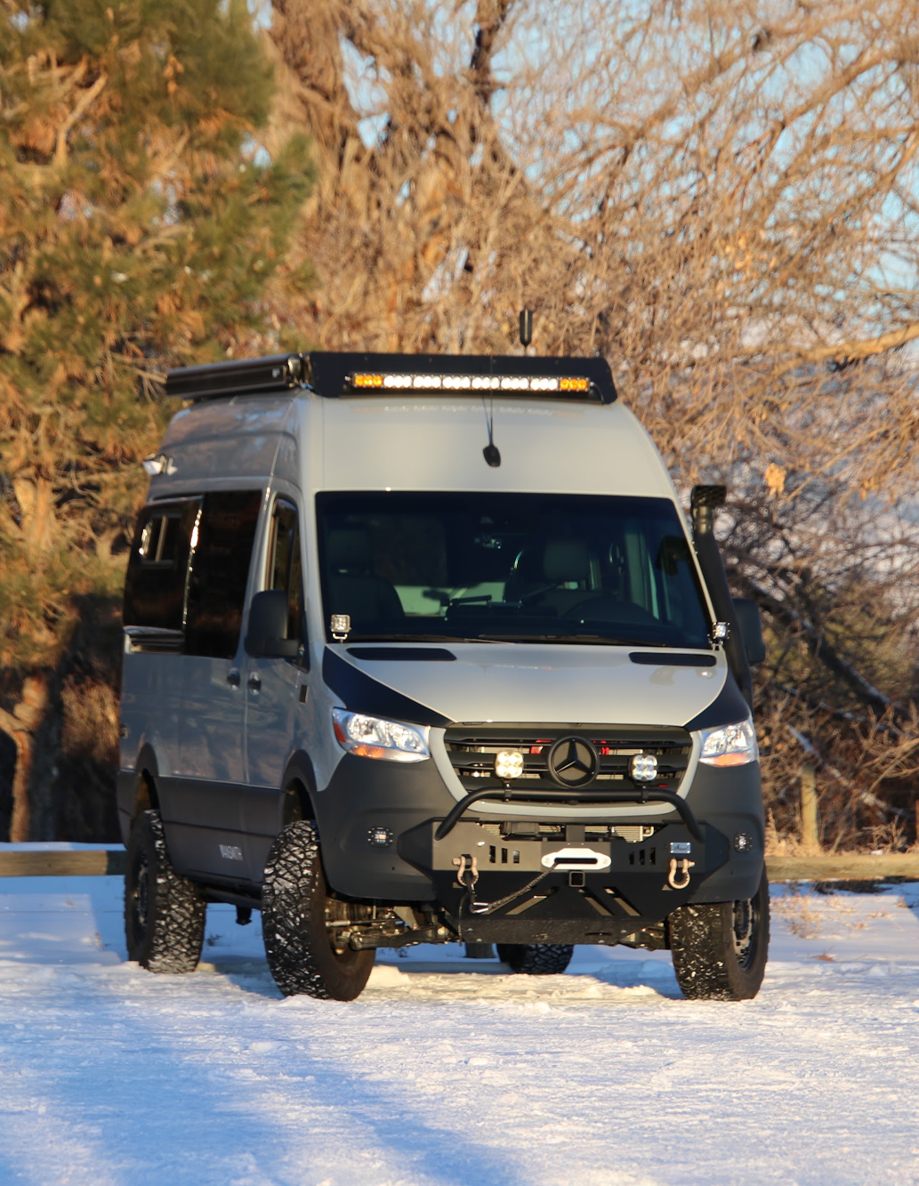 Front of Colorado Sprinter Van Conversion by The Vansmith with Headlights Shining Through Reedgrass