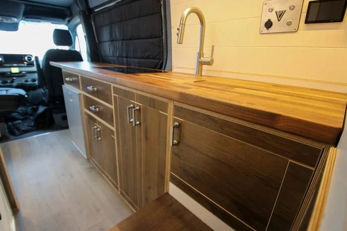 High-End Wood-Finish Kitchen Galley with Stove, Fridge and Sink in Family Van Conversion by The Vansmith