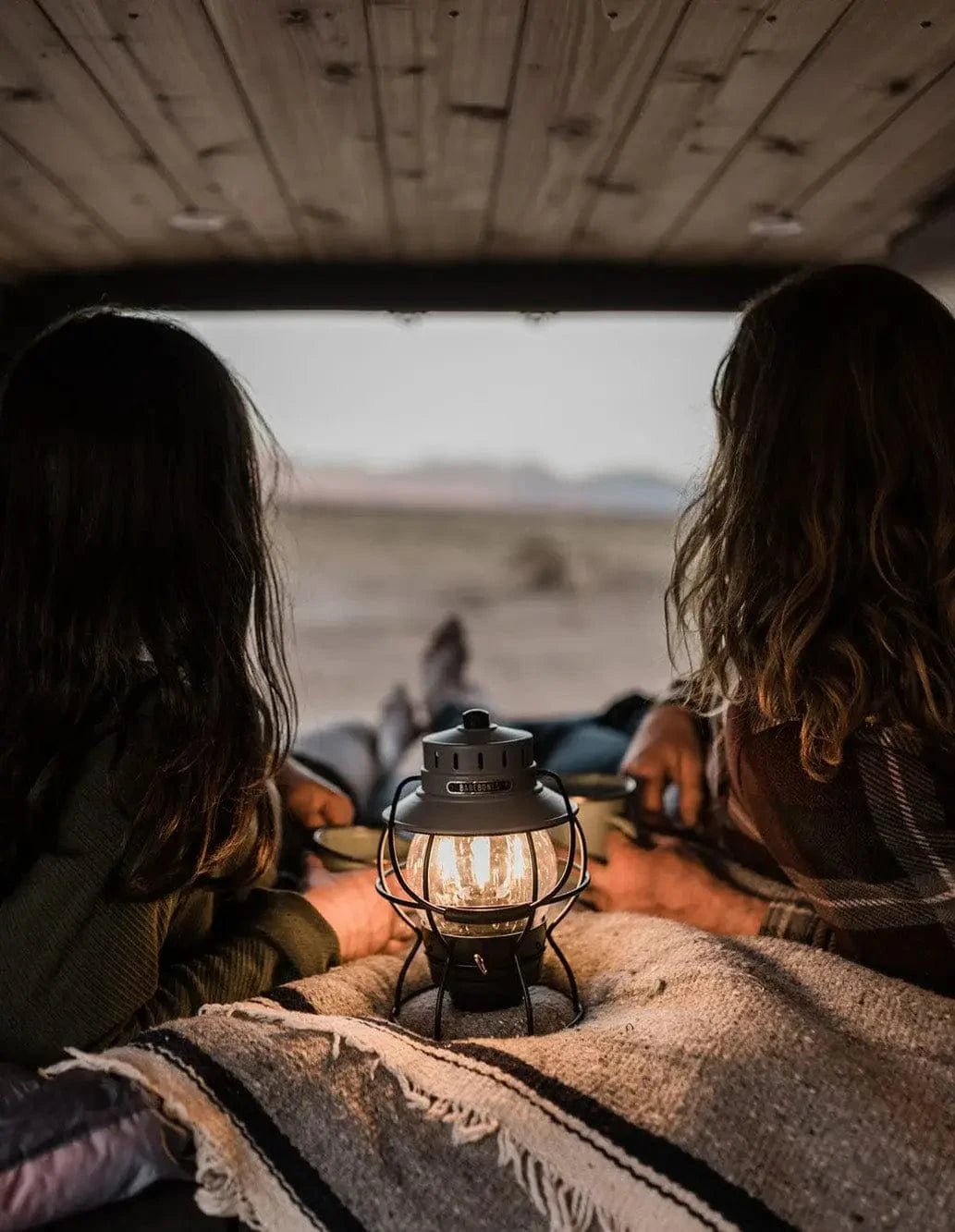 Couple in Bed with Lantern Enjoying Mountain Views from Back of Custom Camper Van by The Vansmith in Colorado