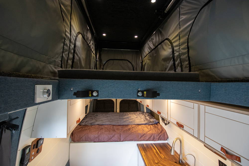 Camper van interior with built-in cabinets, countertop, and sleeping space under pop top