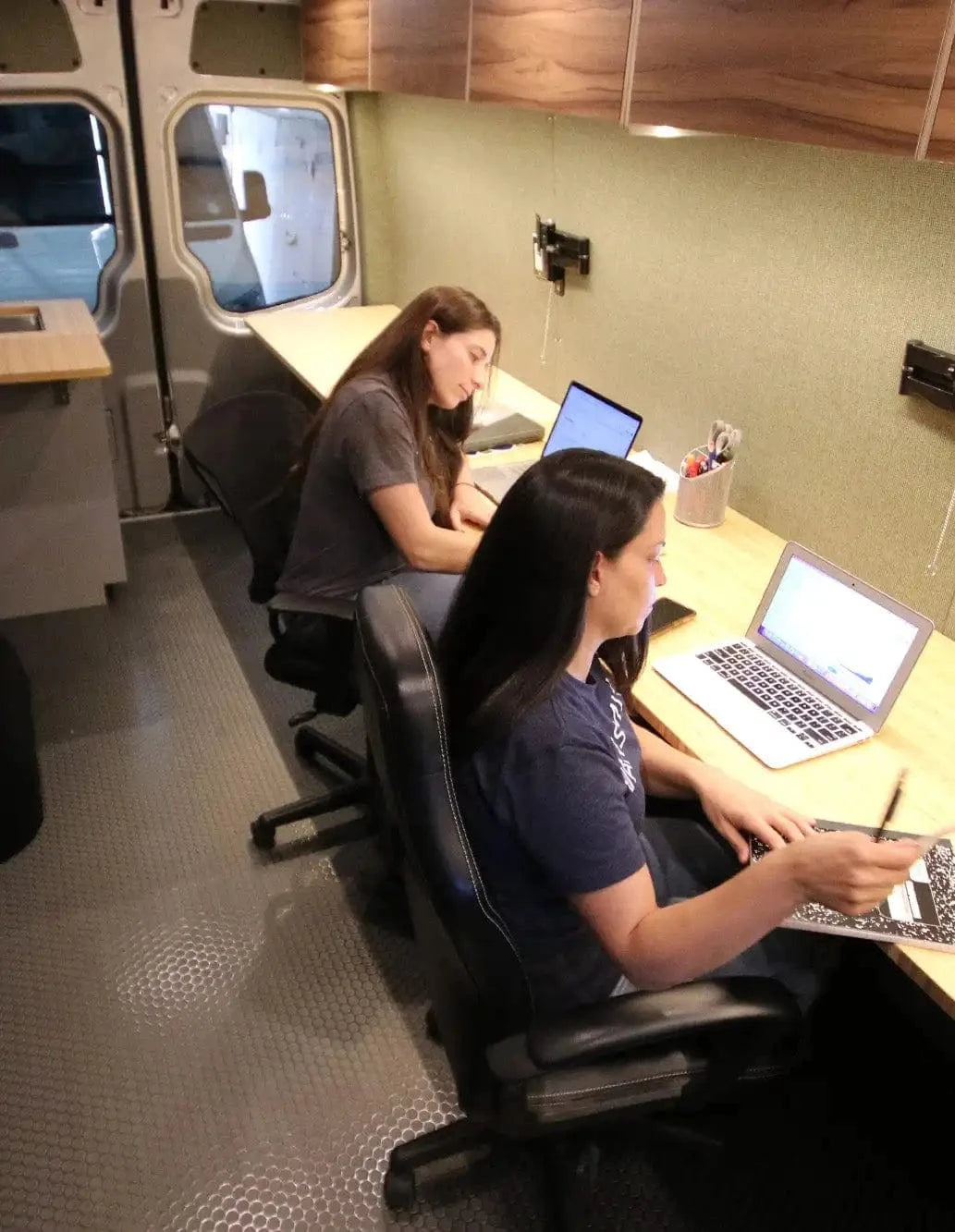 Two Women Working with Laptops at Long Desk in Custom Mobile Office Van Upfitted by The Vansmith