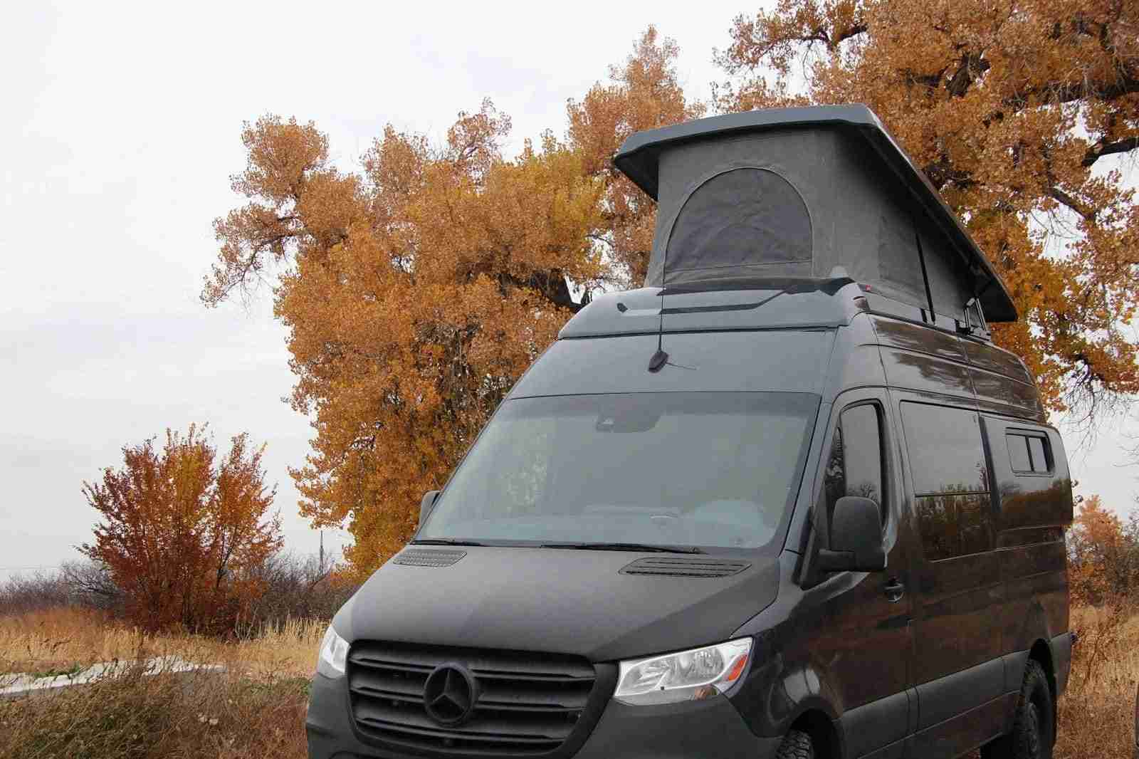 Pop top camper van exterior view showing raised roof at sunset