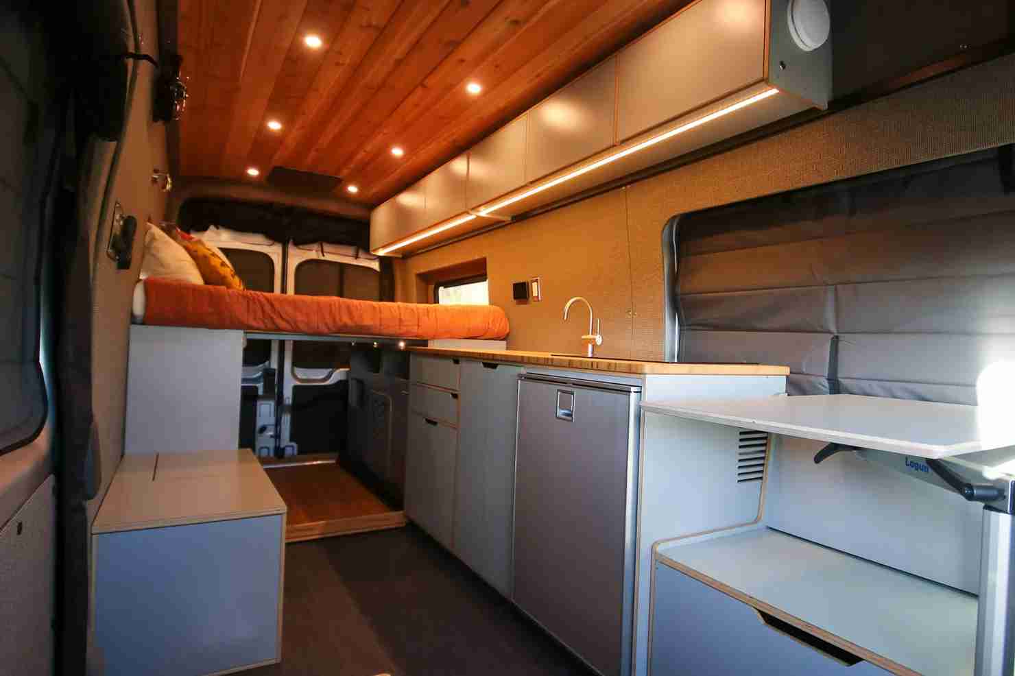 Interior View of Ford Transit Van Conversion by The Vansmith with Raised Bed, Kitchen Galley and Wood Ceiling with Recessed Lighting