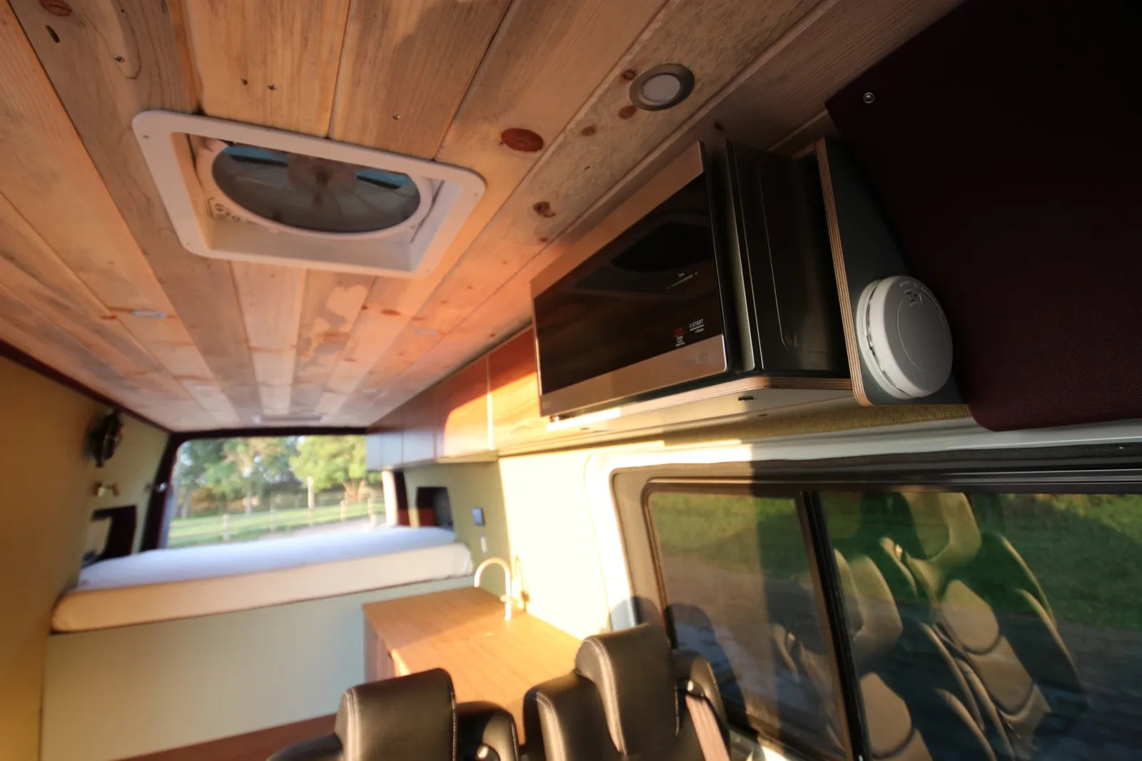 Overhead walnut cabinetry with microwave and roof vent fan in AL Sprinter van conversion