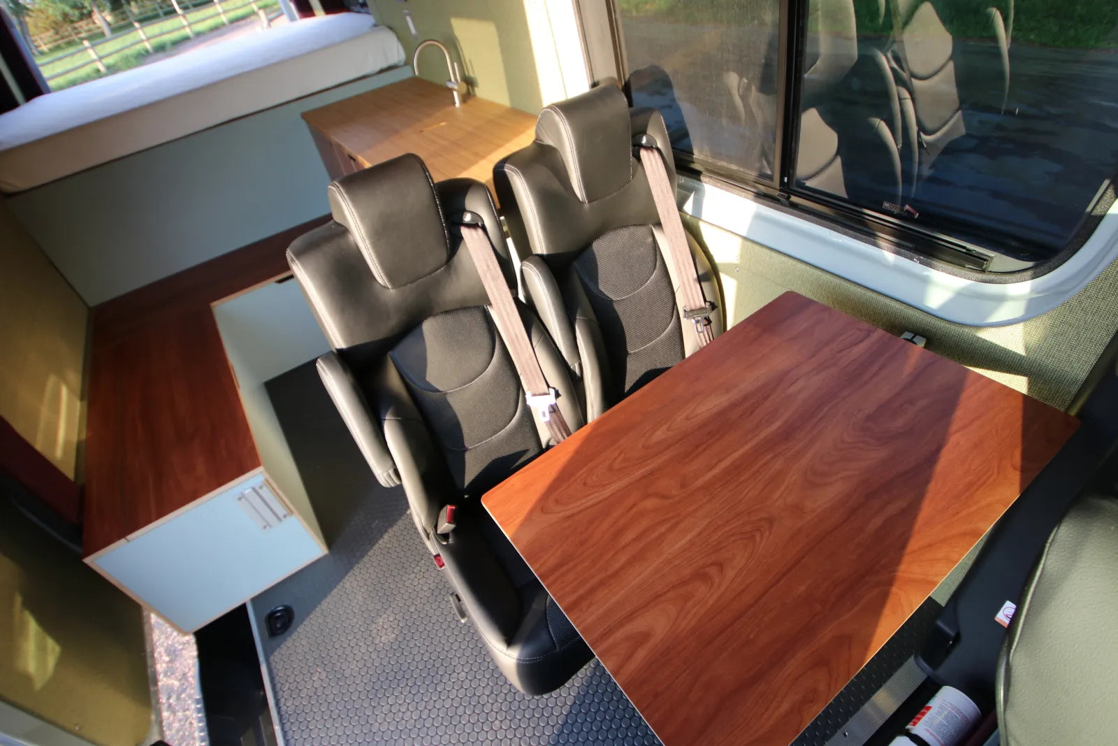 Walnut fold-down dining table with leather captain chairs in AL Sprinter van conversion interior