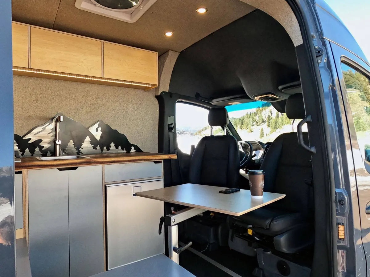 Gina van interior with mountain silhouette art, swivel table, and kitchen area by The Vansmith