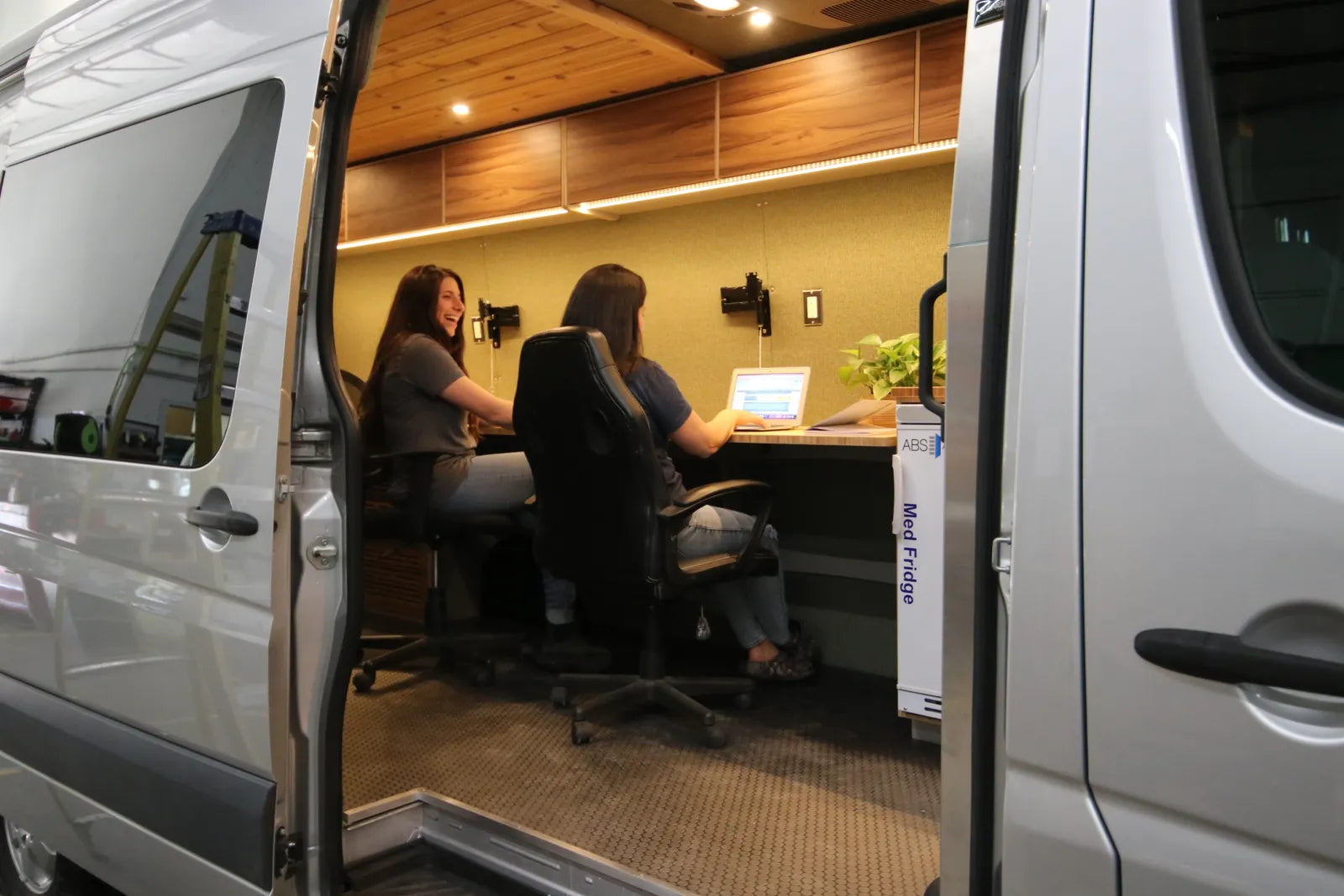 Hustle mobile office Sprinter van with two people working at laptops through sliding door by The Vansmith