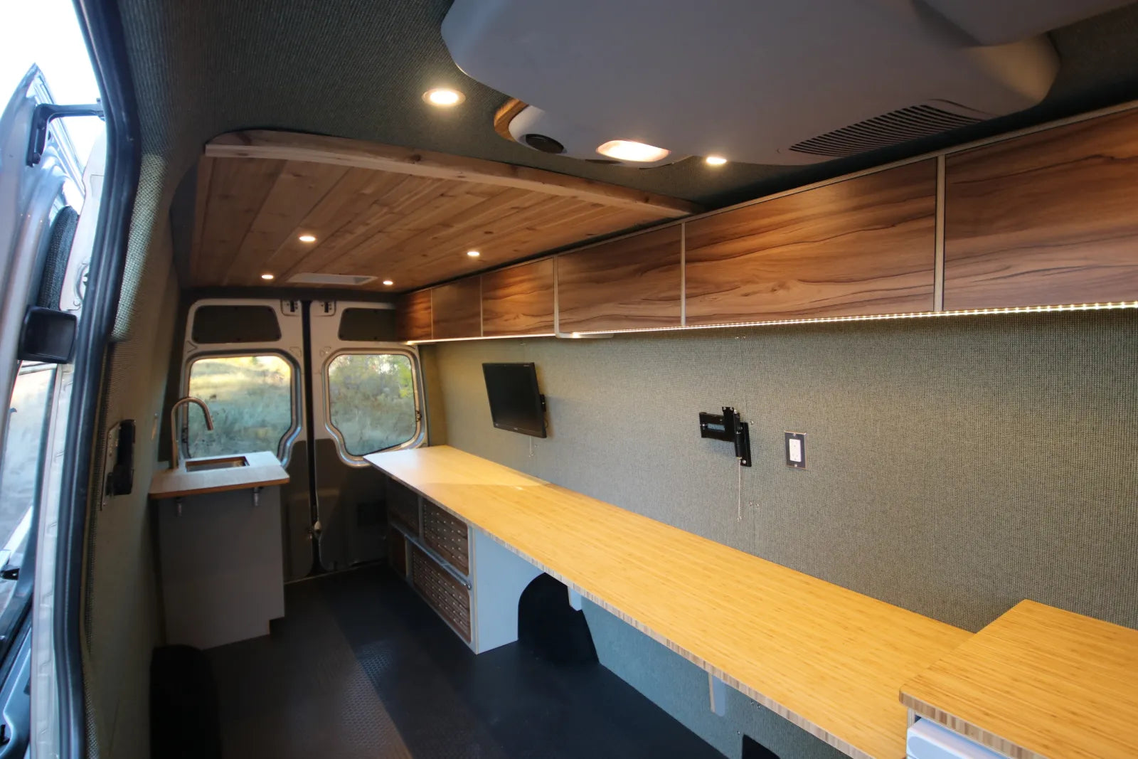 Hustle Sprinter van interior with overhead walnut cabinets LED lighting and long workspace by The Vansmith
