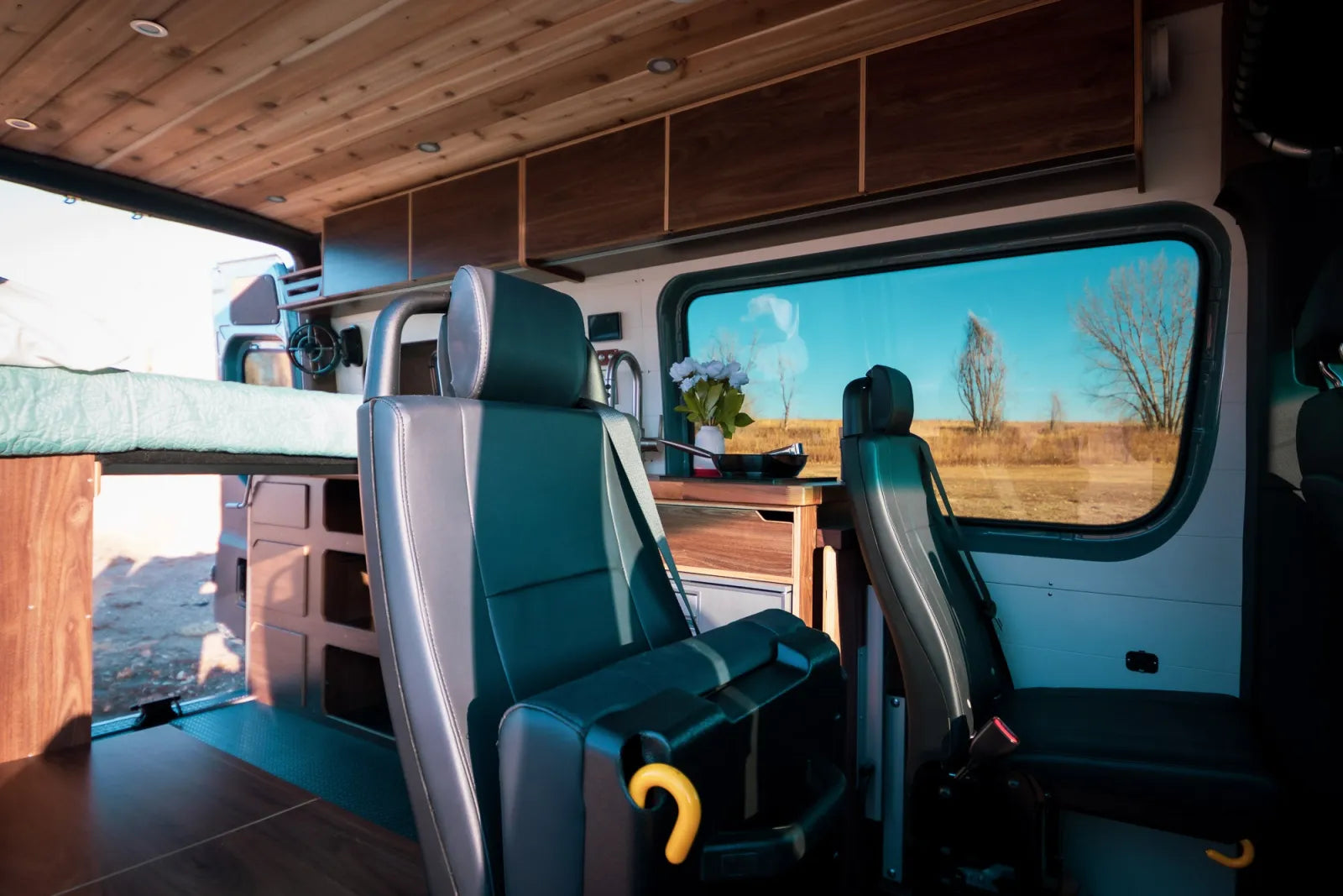 Jimmy van conversion rear-facing seats with teal upholstery and overhead cabinets by The Vansmith