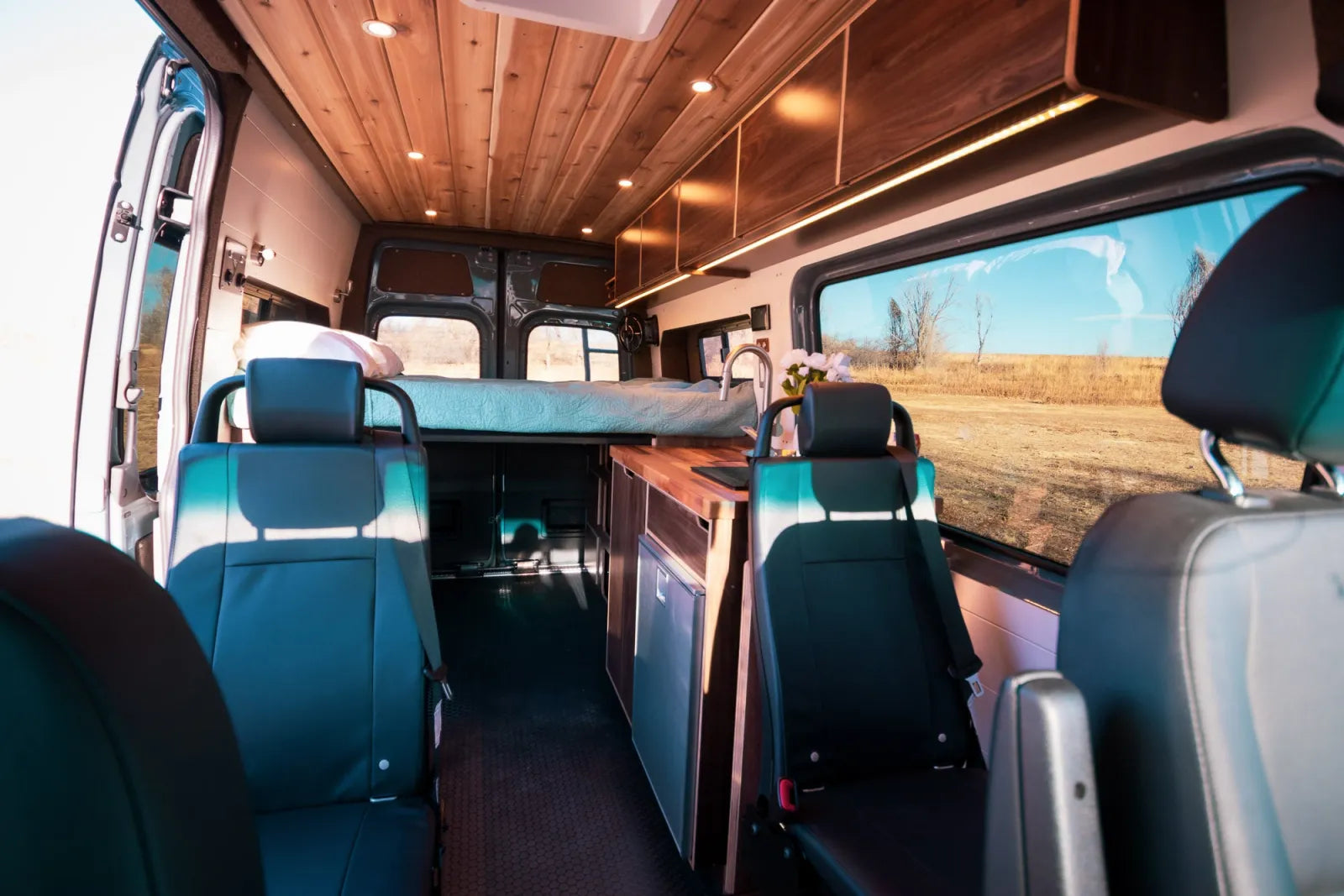 Jimmy Sprinter van interior looking forward with four seats and elevated bed platform by The Vansmith