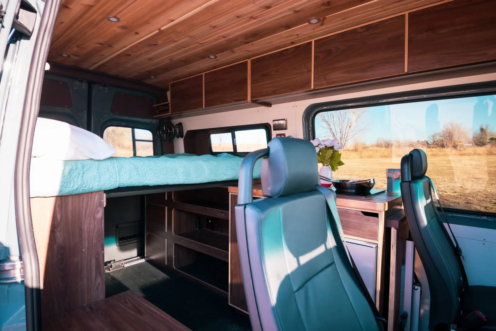 Jimmy van conversion interior with teal seats overhead walnut cabinets and bed area by The Vansmith