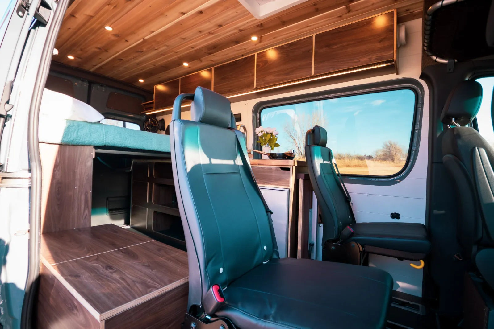 Jimmy Sprinter van interior with swivel seats overhead storage and elevated bed by The Vansmith