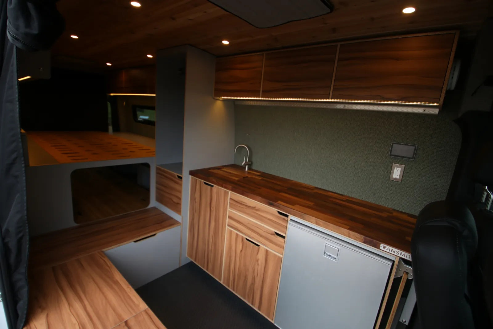 Maverick Sprinter van conversion kitchen with walnut countertop sink overhead cabinets and fridge by The Vansmith