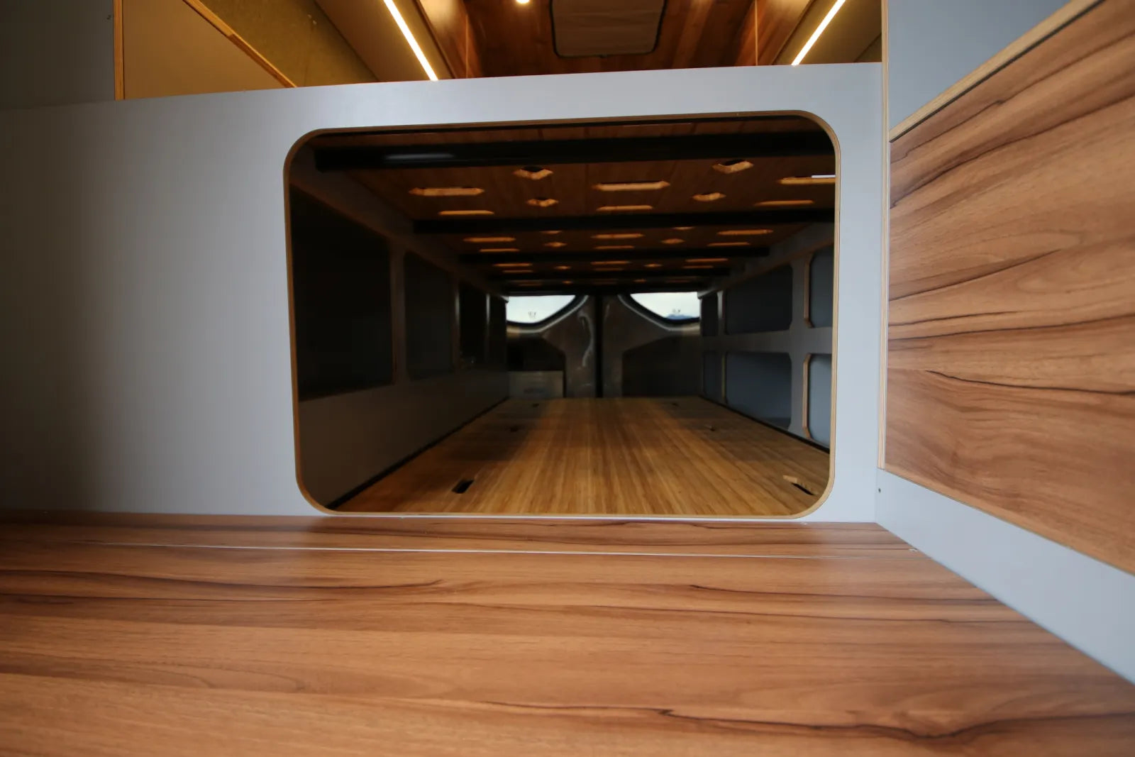 Maverick Sprinter van under-bed storage area with walnut panels and rounded cutout by The Vansmith