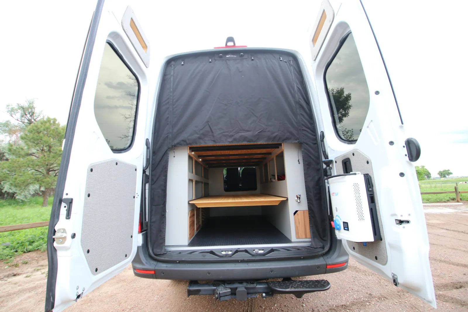Maverick Sprinter van rear doors open showing bed platform insulated curtains and storage by The Vansmith
