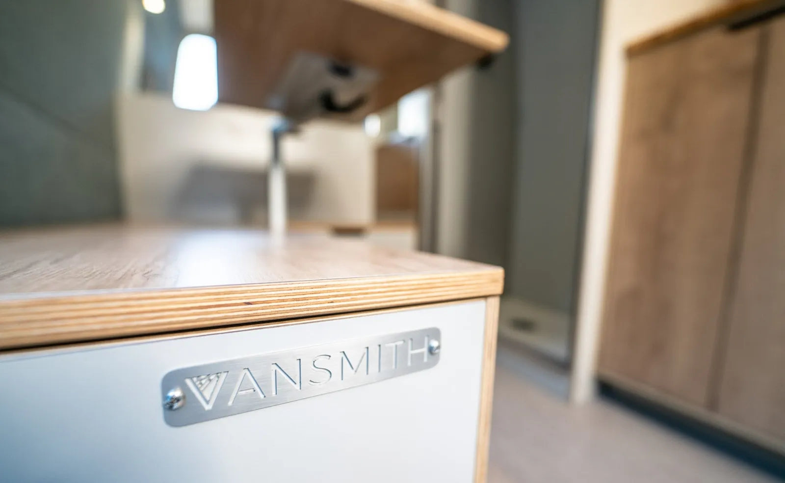 The Vansmith metal badge close-up on custom cabinetry in Outpost van