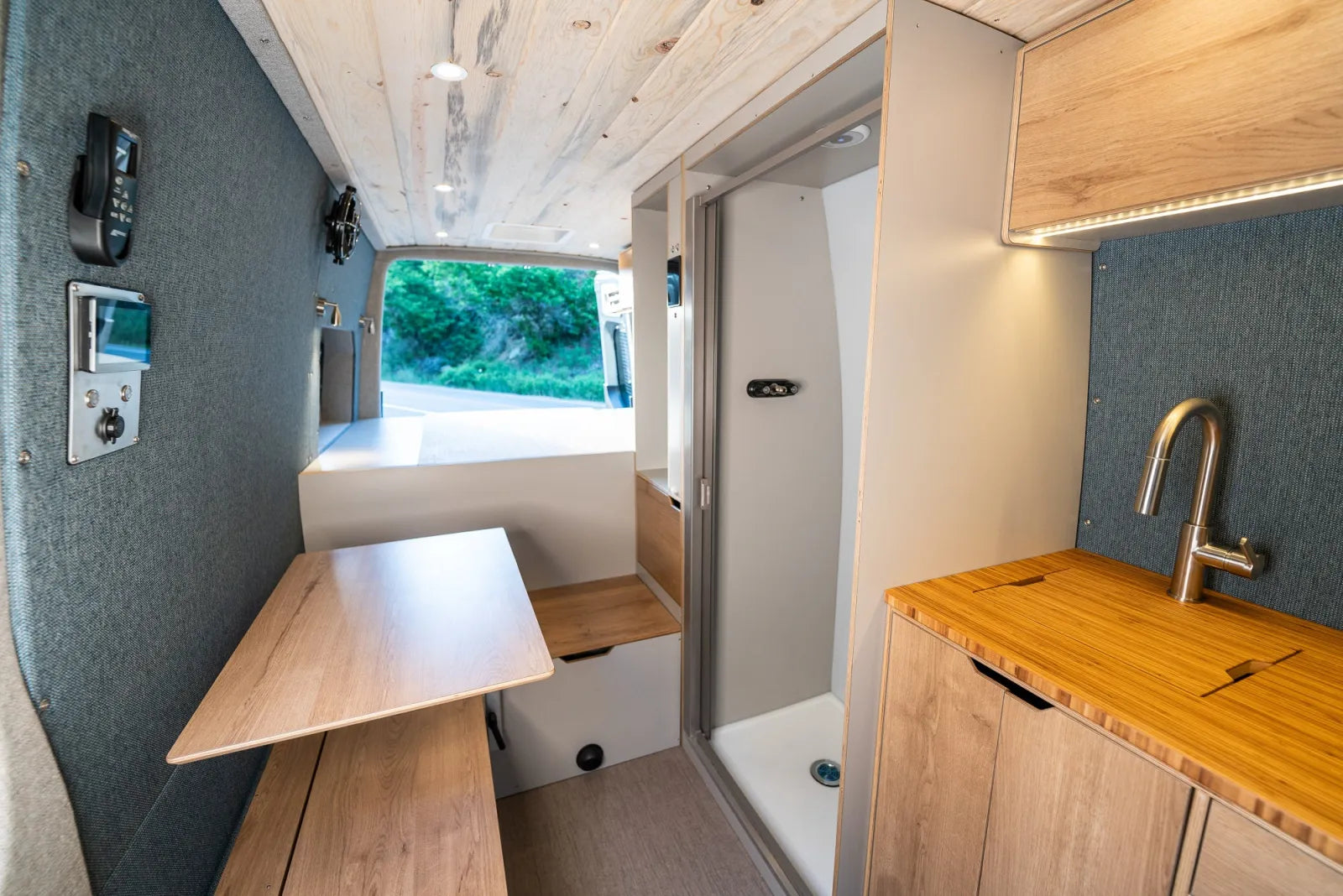 Outpost van interior with electrical panel, fold-up table, and kitchen galley