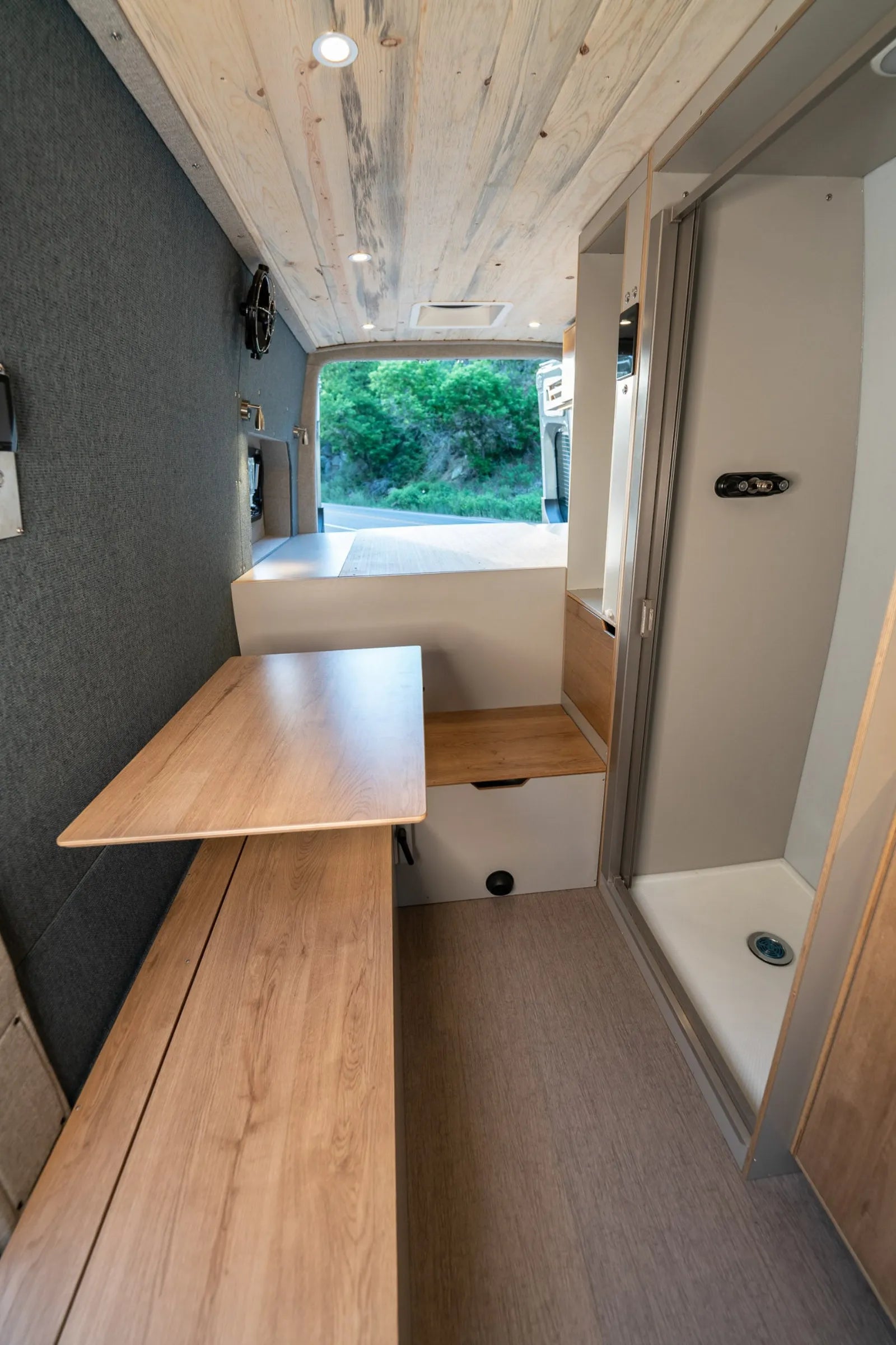 Outpost van dinette area with fold-down table, bench, and shower visible