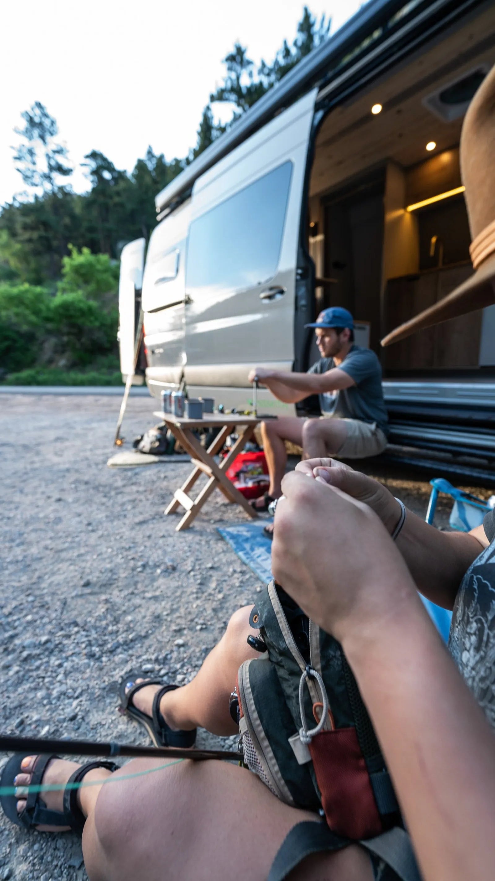 Couple relaxing outside Outpost Sprinter van conversion at campsite