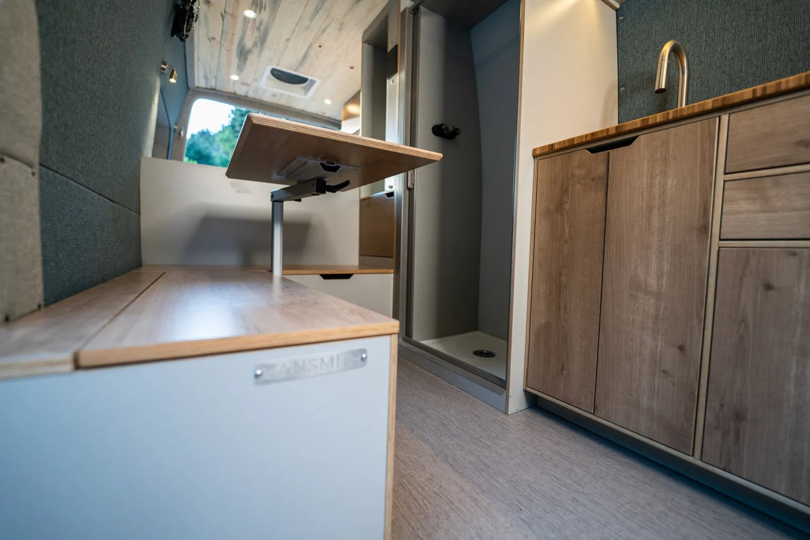 Outpost van interior with adjustable pedestal table and kitchen cabinetry