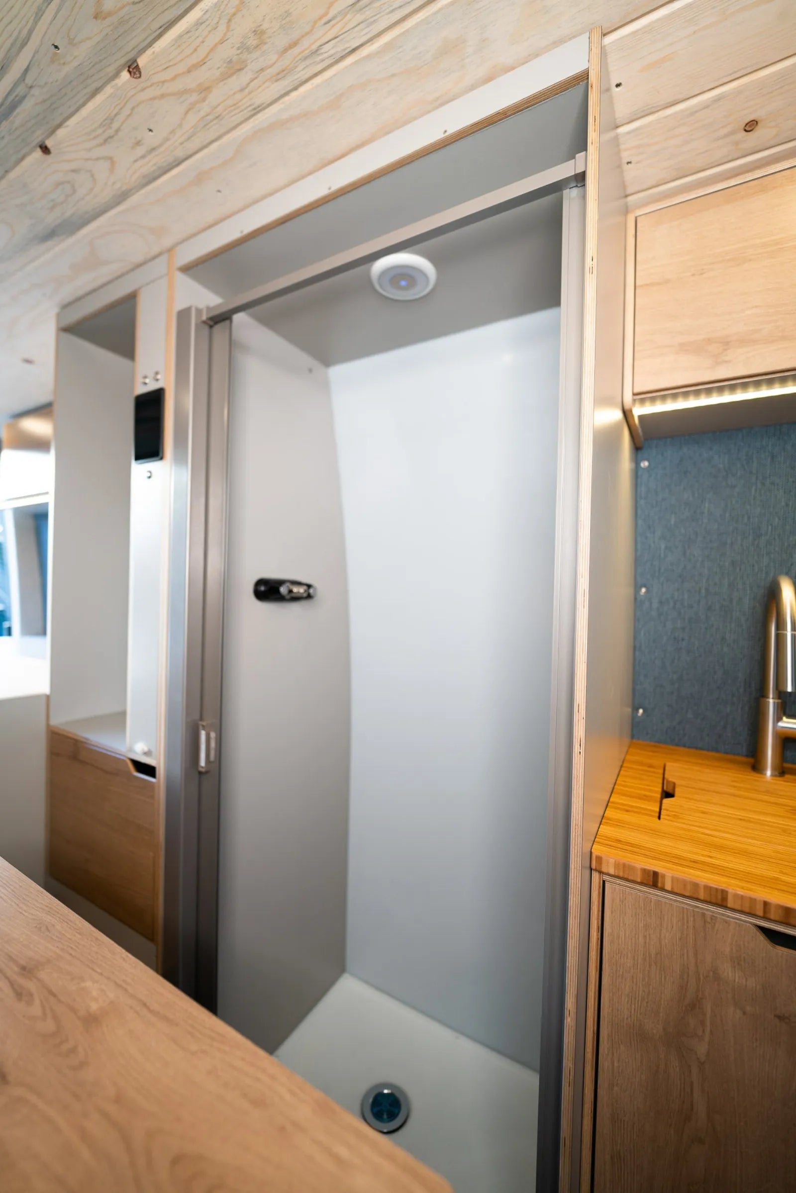 Enclosed shower with sliding door and sink in Outpost Sprinter van conversion