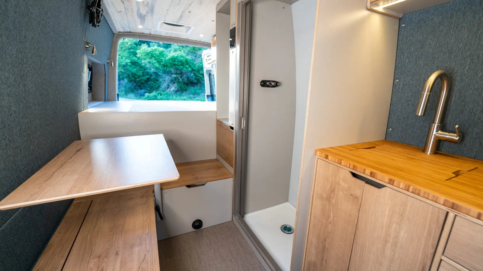 Outpost van interior with fold-up dinette, kitchen sink, and oak cabinetry