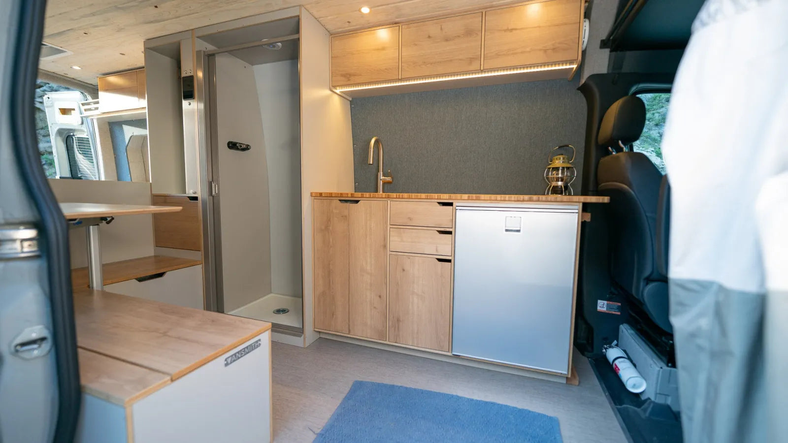 Outpost van kitchen with oak cabinets, sink, fridge, and enclosed shower stall