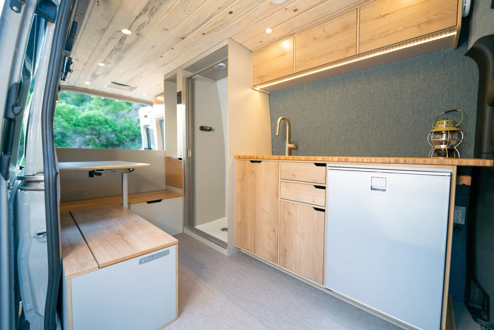 Outpost van galley kitchen with oak cabinetry, gold faucet, and shower door
