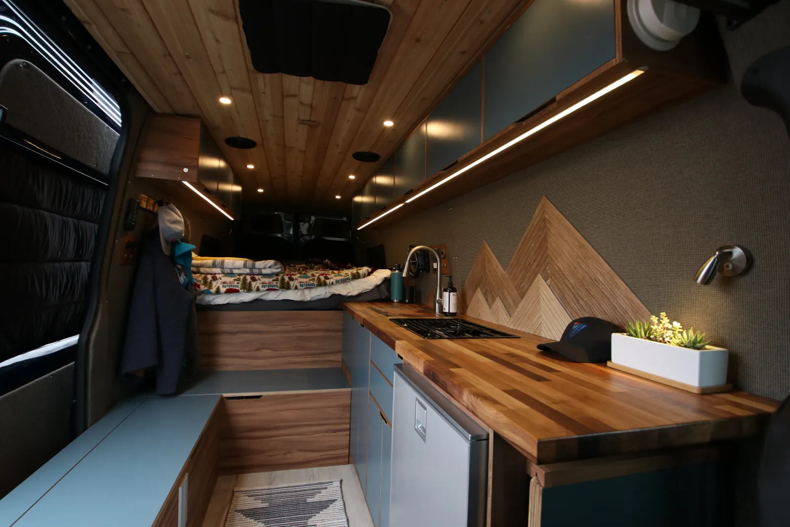 Rapp van interior with walnut counters, mountain backsplash, bed, and cooktop