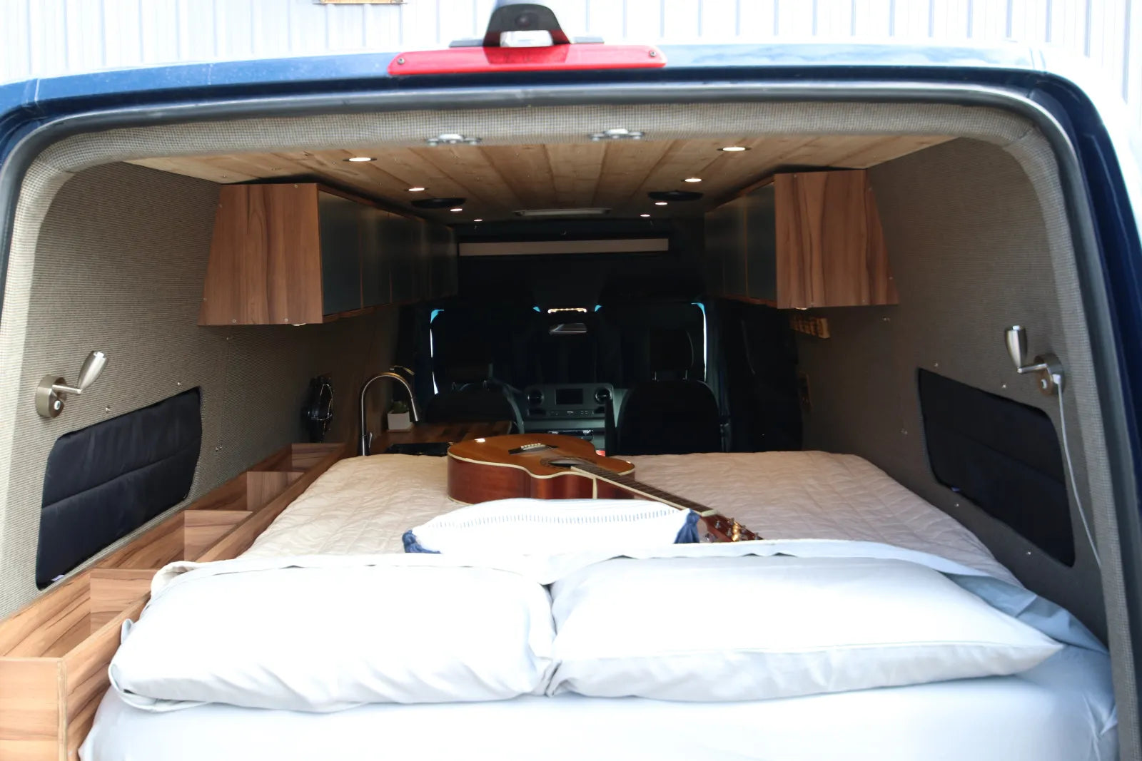 Rapp Sprinter rear with bed extended, pillows, guitar, and overhead cabinets