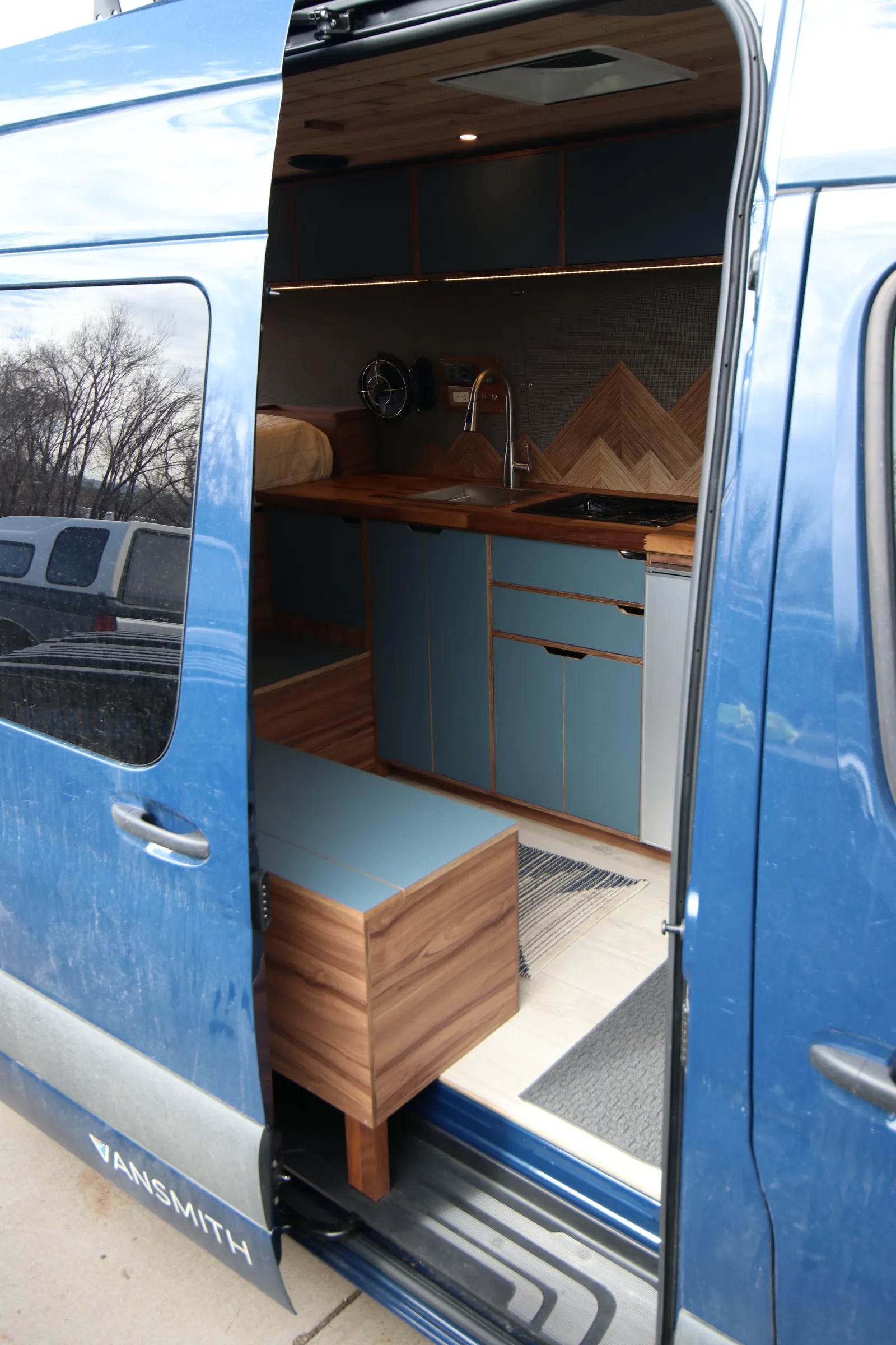 Rapp blue Sprinter side door view showing kitchen and walnut bench seating