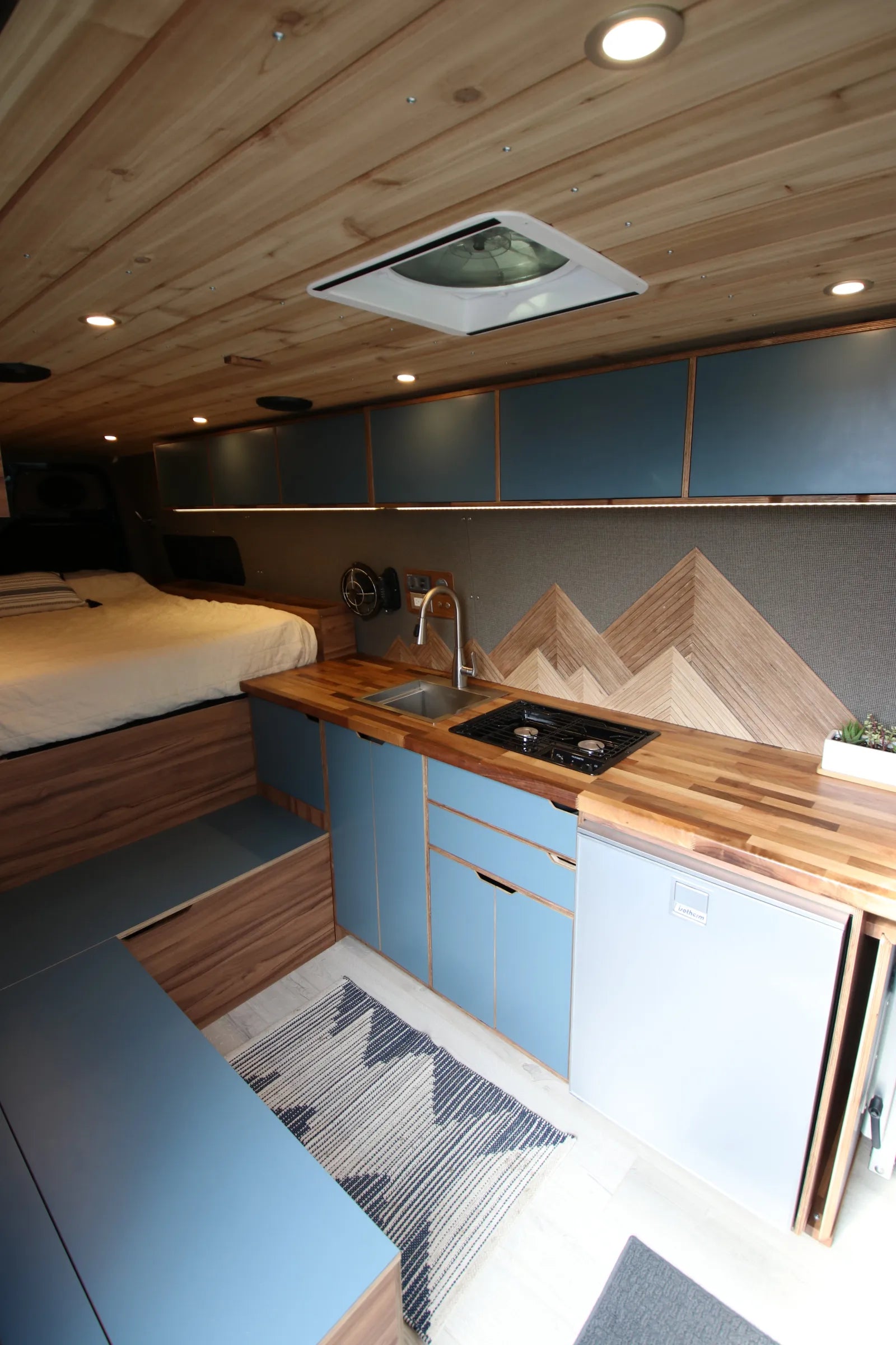 Rapp van kitchen with blue cabinets, walnut counter, cooktop, and MaxxFan