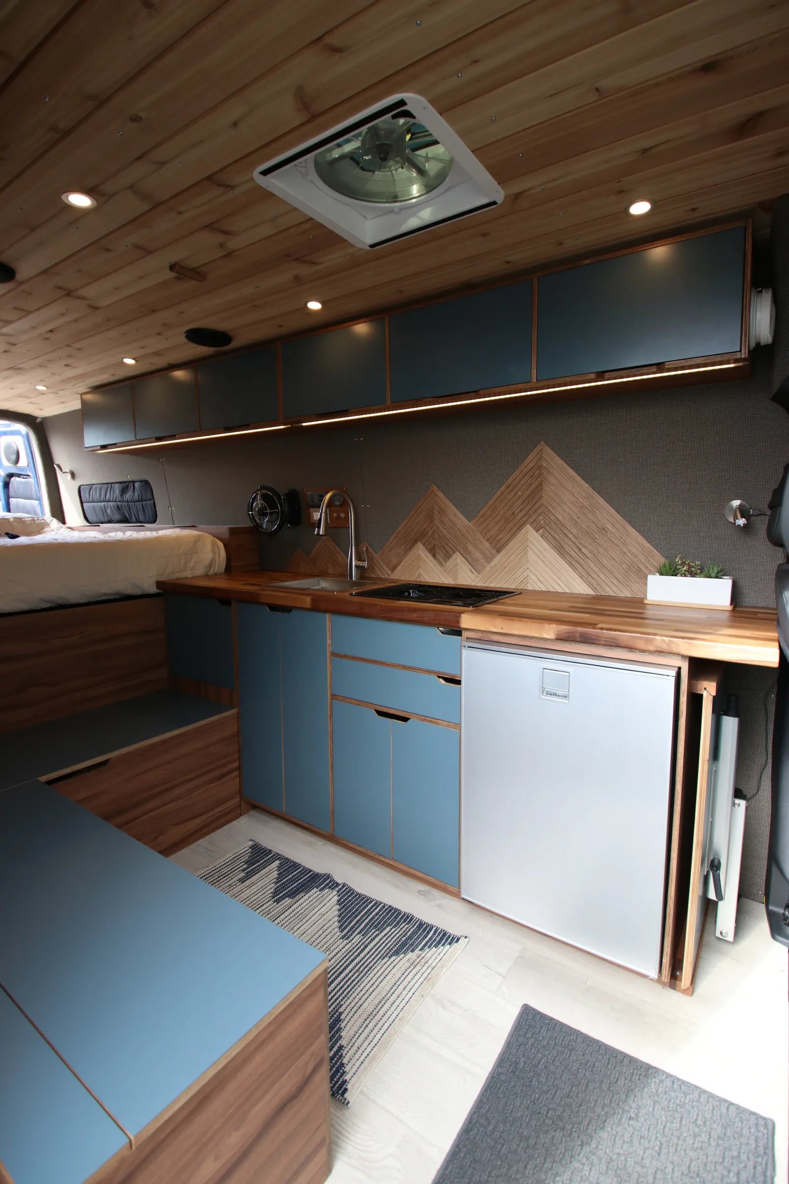 Rapp van kitchen galley with blue cabinets, mountain backsplash, and fridge