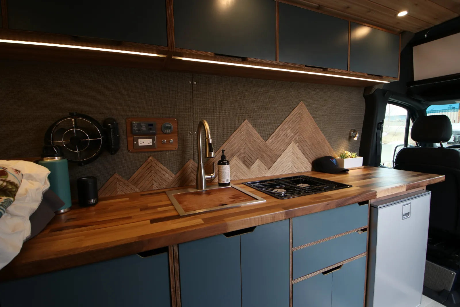 Rapp van kitchen with walnut countertop, cooktop, sink, and mountain art