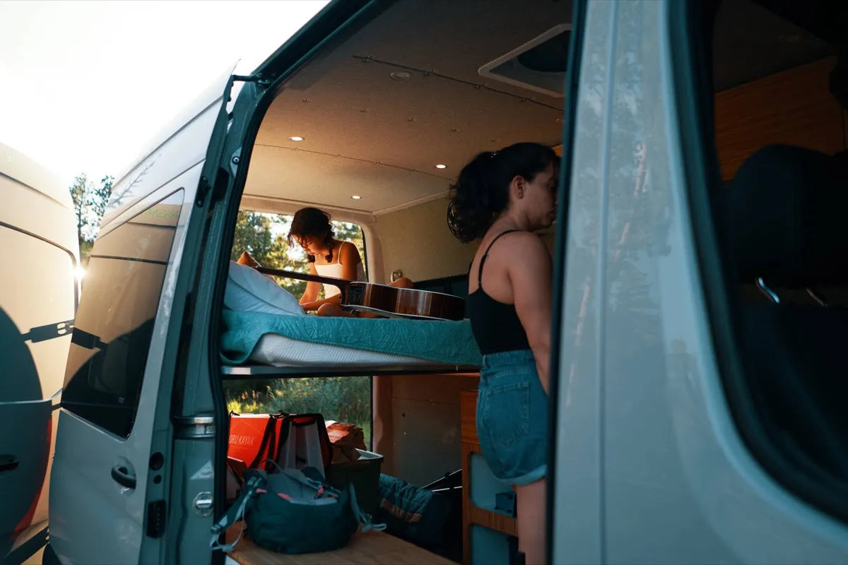 Scout Sprinter van conversion lifestyle with person playing guitar on floating bed at sunset by The Vansmith