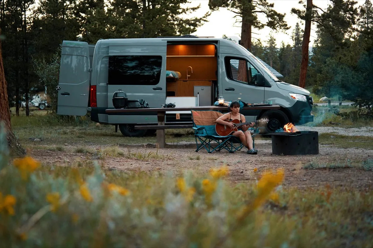 Scout Sprinter 144 camper van at campsite with person playing guitar by campfire at dusk by The Vansmith